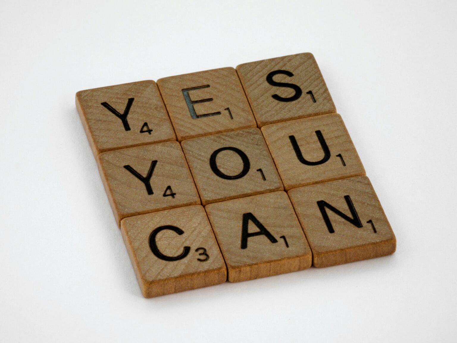 Wooden Scrabble tiles on white surface spelling 'Yes You Can,' promoting positivity and motivation.